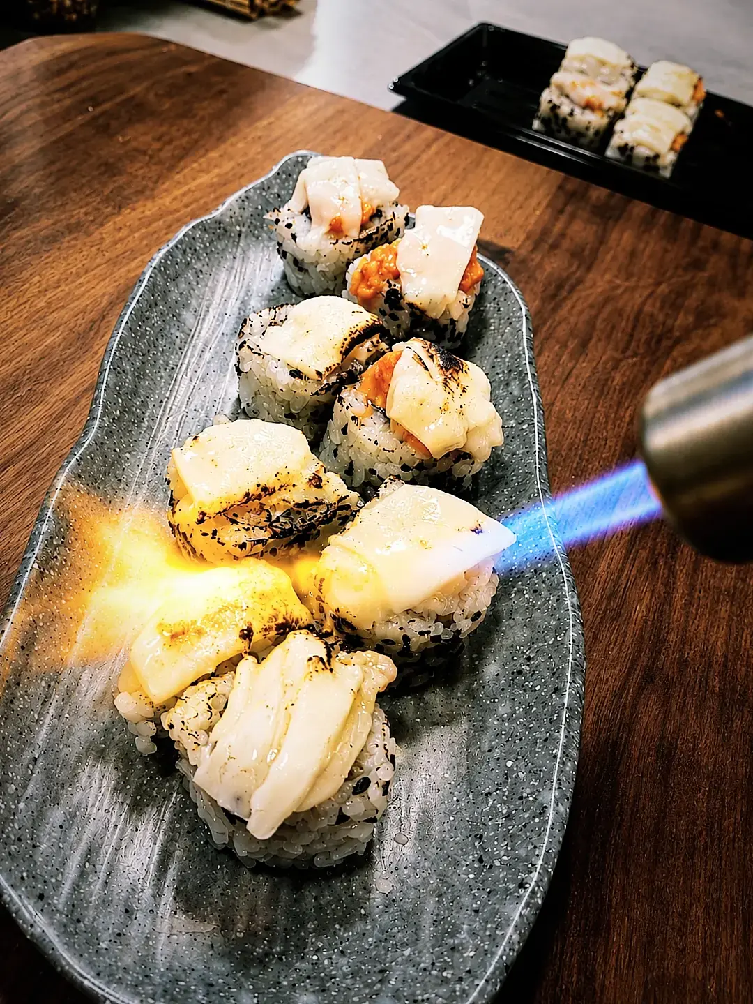 Un bufador flameja uramakis de salmó en un plat de pedra.