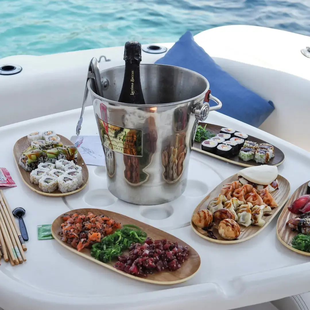 Una taula de barca amb sushi, gyozes i cava en gel, amb el mar de l’Ametlla al fons.